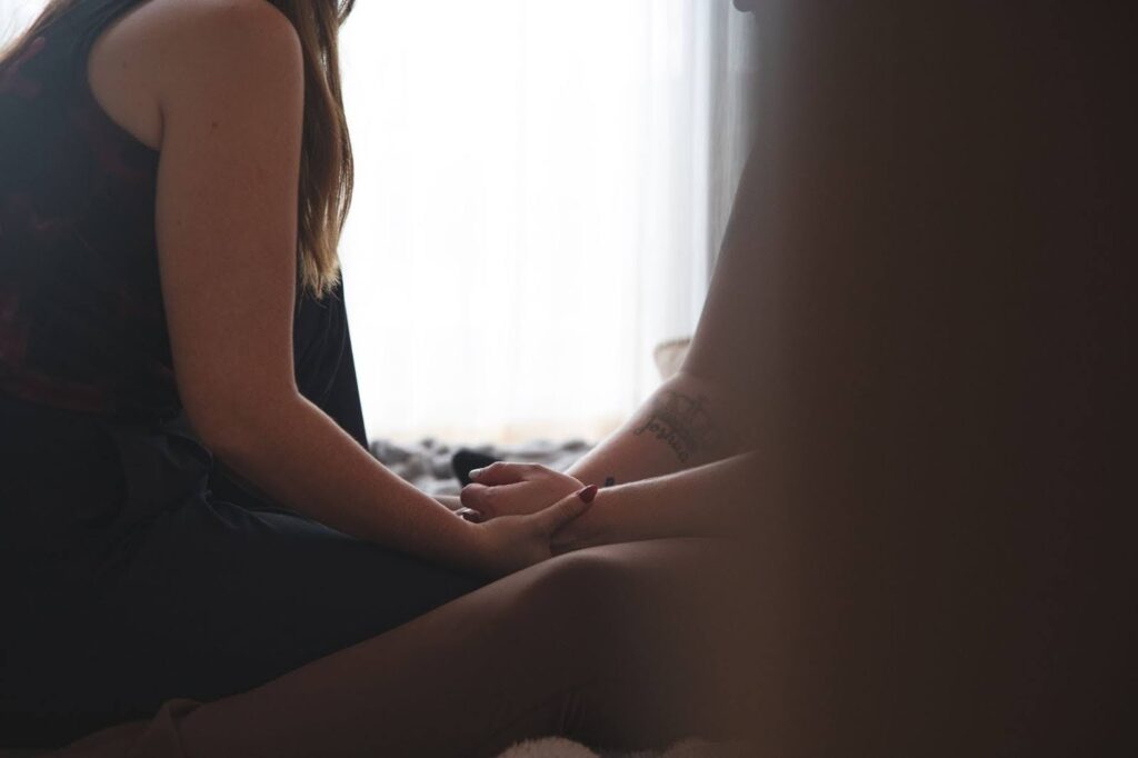 close up image of two people sitting cross legged and facing each other, holding hands.  you cannot see their faces. 